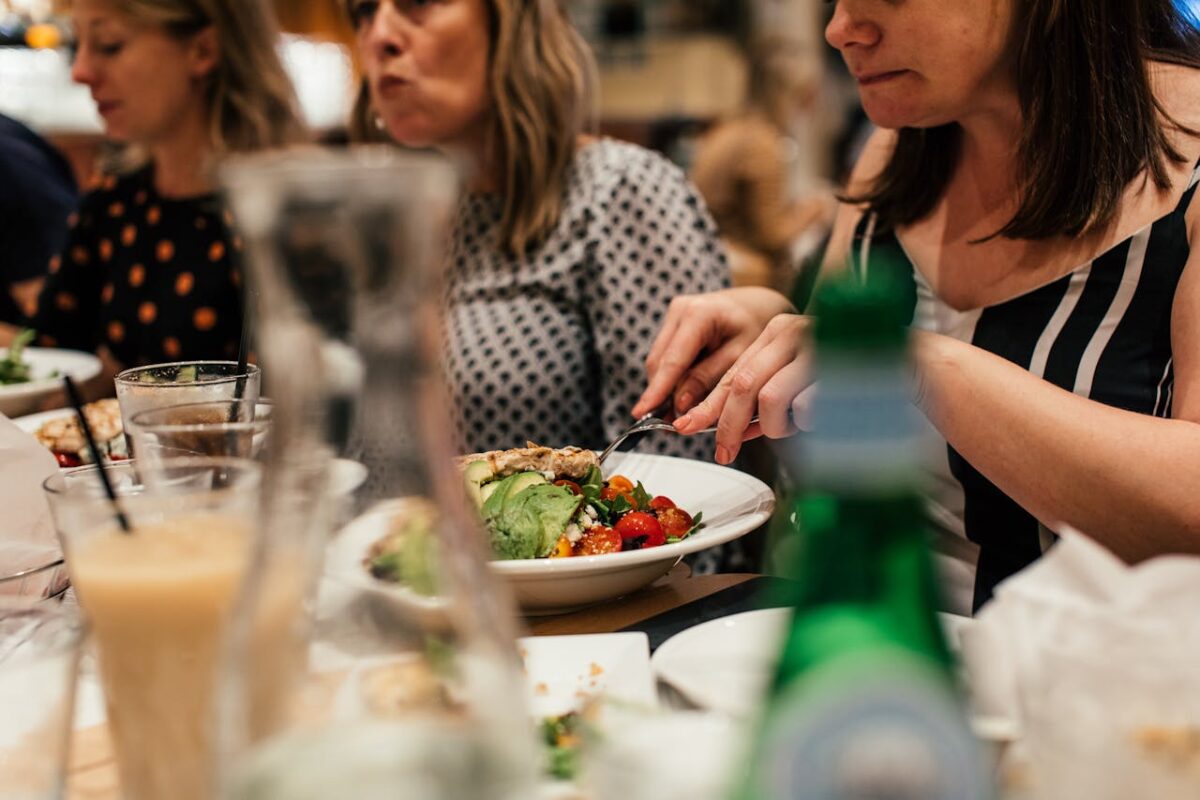 Friends sharing a lively meal at a restaurant, featuring fresh salads and drinks.